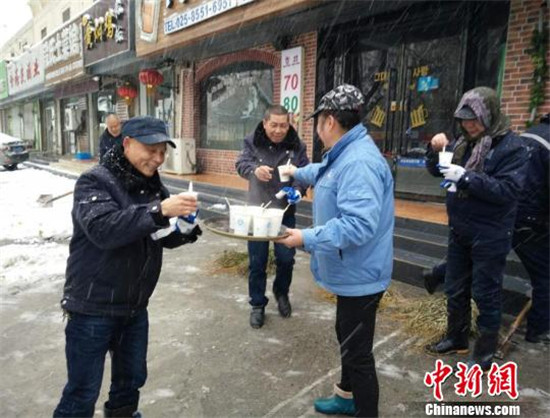 街道周围的店家送来热饮给扫了一早上雪的城管工作人员暖暖身体。朱薇洁 摄